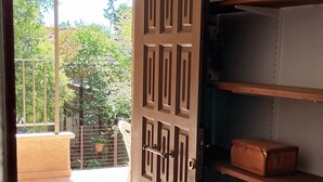 Une porte ouverte donne sur un balcon d’où l’on peut admirer des arbres et un immeuble. À l’intérieur, on trouve un radiateur, une étagère avec une boîte et un sol carrelé.