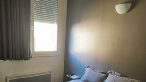 A hotel room with a bed, a window with blinds, a bedside table, and a wall-mounted light. - Hôtel de la Gare (Périgueux)