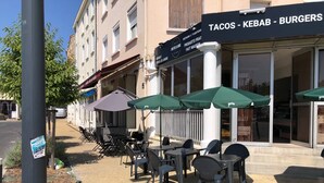 Outdoor seating with tables and chairs, a building with a sign advertising tacos, kebabs, and burgers, and a clear sky. - Hôtel de la Gare (Périgueux)