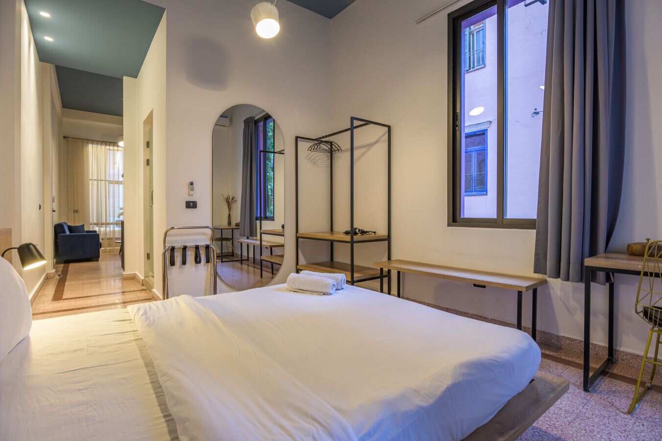 Quarto de hotel moderno com uma cama grande, uma escrivaninha, uma cadeira e um espelho.
