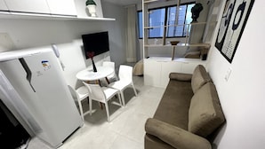 A compact living space with a kitchenette, a dining area with a table and chairs, a sofa, and a view of the city through a window.