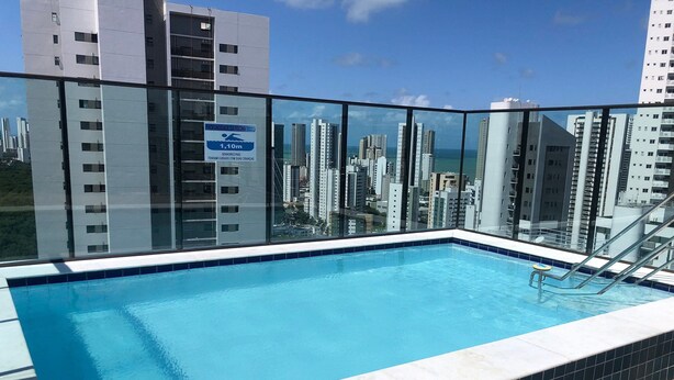 A rooftop pool with a glass barrier, surrounded by high-rise buildings.