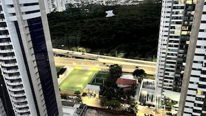 A high-rise building with multiple balconies, a sports field, and a road with vehicles.