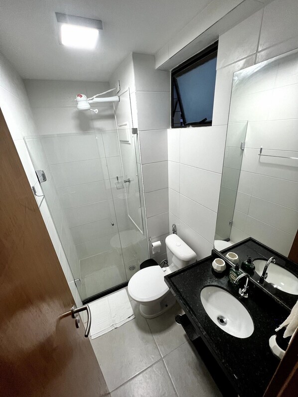 Un baño moderno con cabina de ducha de vidrio, inodoro, lavabo con espejo y ventana sobre el inodoro.