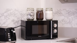 A black microwave oven with three glass jars on top, a toaster, and a stainless steel sink. - Birmingham City Centre Apartment, Free Parking (Birmingham)