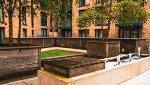 A courtyard with wooden benches, a small grassy area, and a water feature. - Birmingham City Centre Apartment, Free Parking (Birmingham)