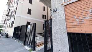 Um edifício residencial de vários andares com entrada fechada por portão, uma parede de tijolos com pichações e uma motocicleta estacionada.