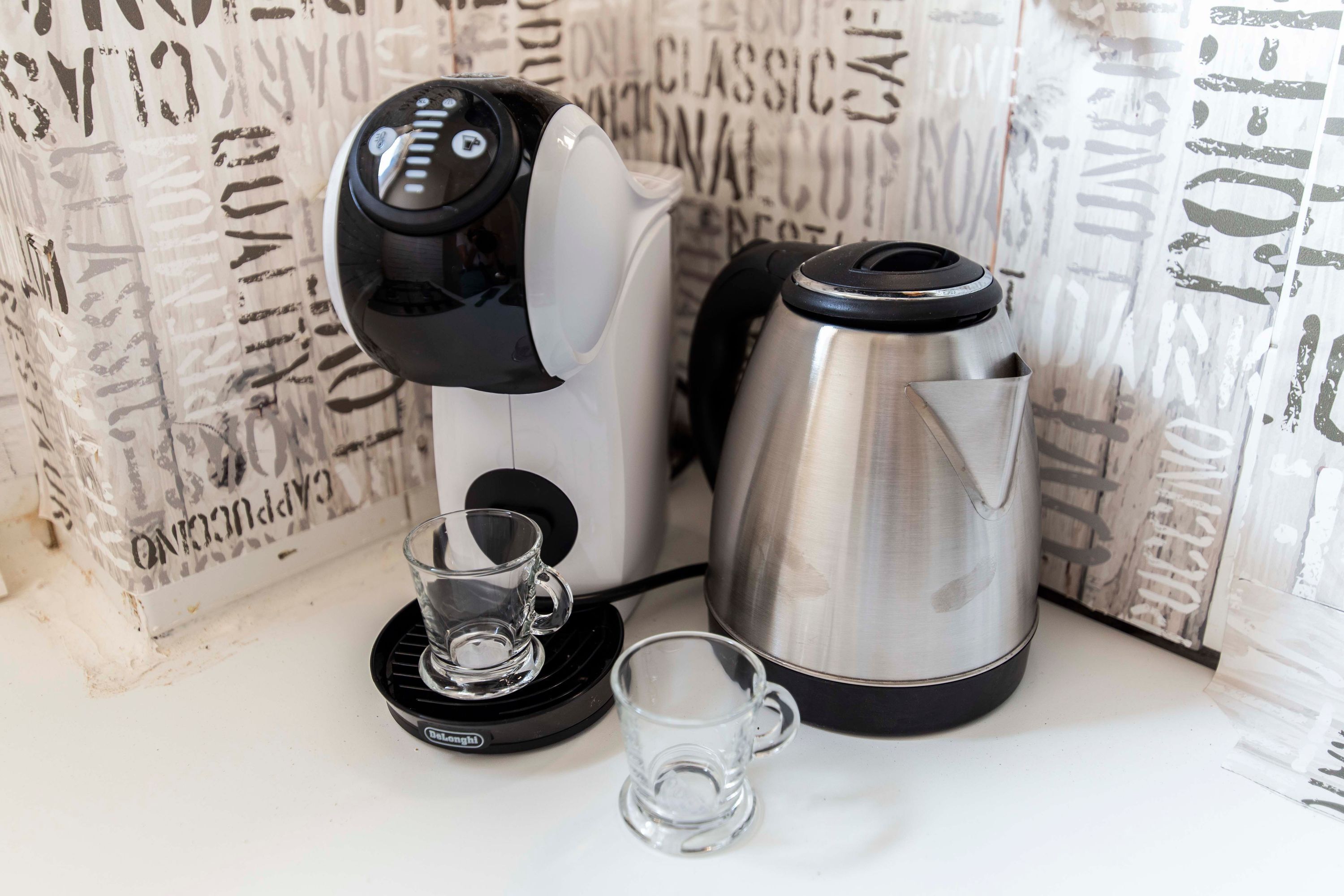 Een koffiezetapparaat, een RVS-waterkoker en twee glazen op een witte aanrechtblad.