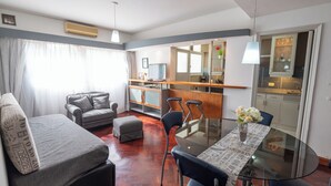 A modern hotel room with a sofa, a dining table with chairs, a small kitchen area, and a bathroom visible through an open door. - Plaza Independencia Mendoza Sol y Nieve  (Mendoza)