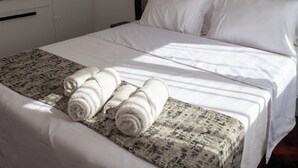 A neatly made bed with white linens and rolled towels, a patterned rug, and a headboard with a textured design. - Plaza Independencia Mendoza Sol y Nieve  (Mendoza)