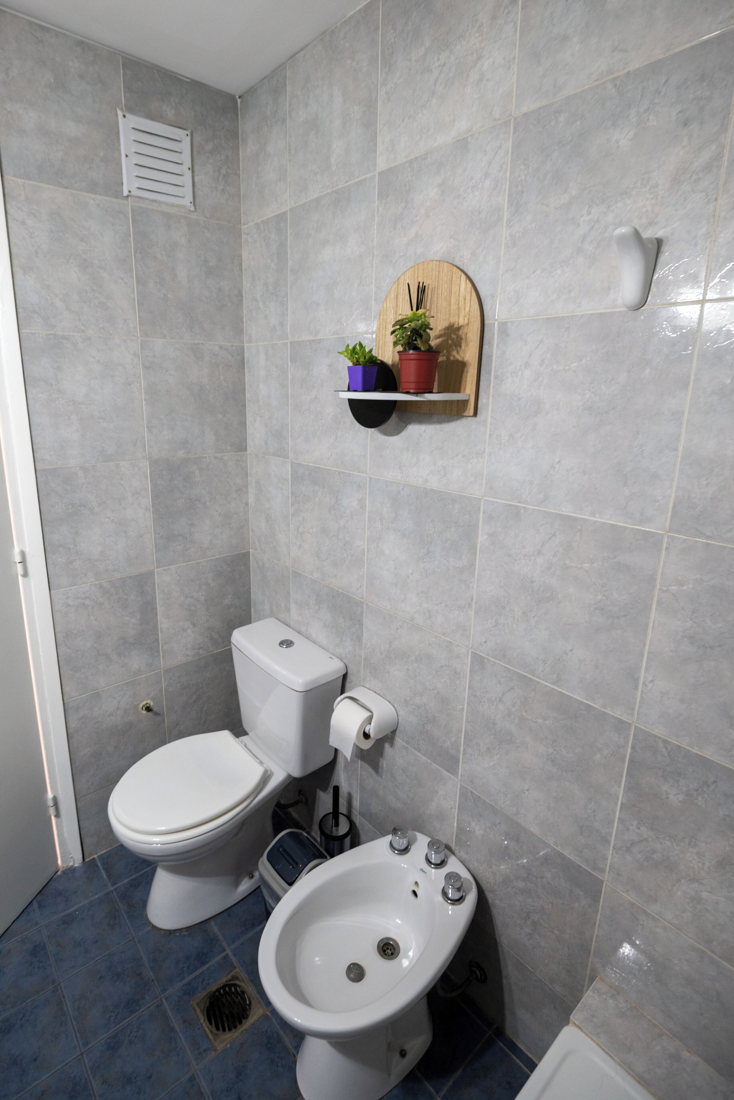 Un baño con inodoro, bidé y una estantería con una planta en maceta.