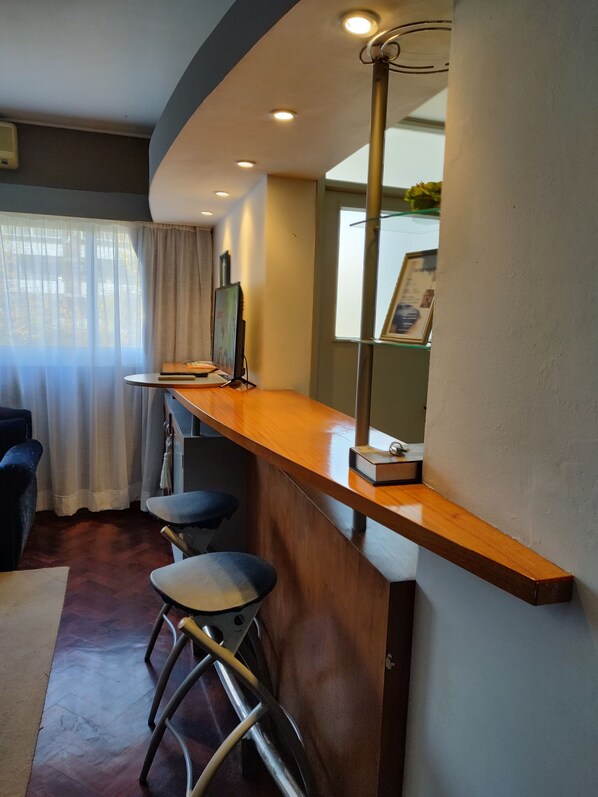 Zona bar moderna con bancone in legno, sgabelli da bar e lampadario.