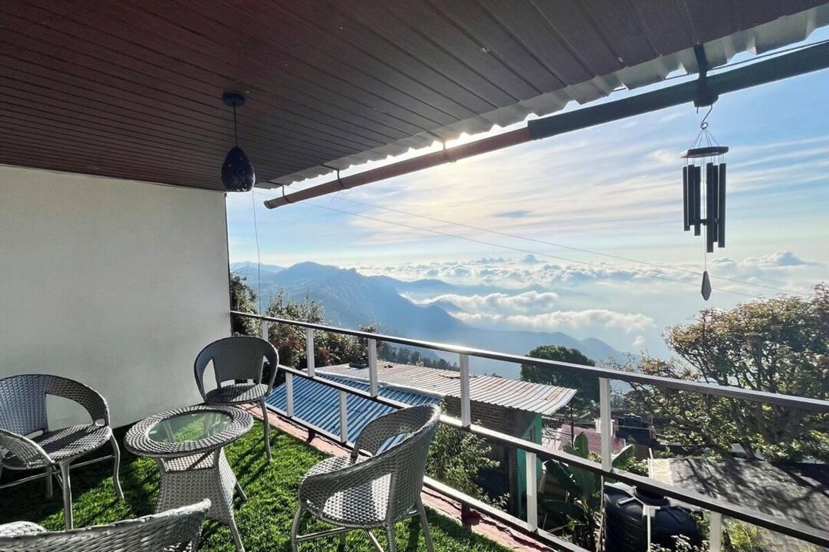 A balcony with wicker furniture and a view of mountains and clouds.