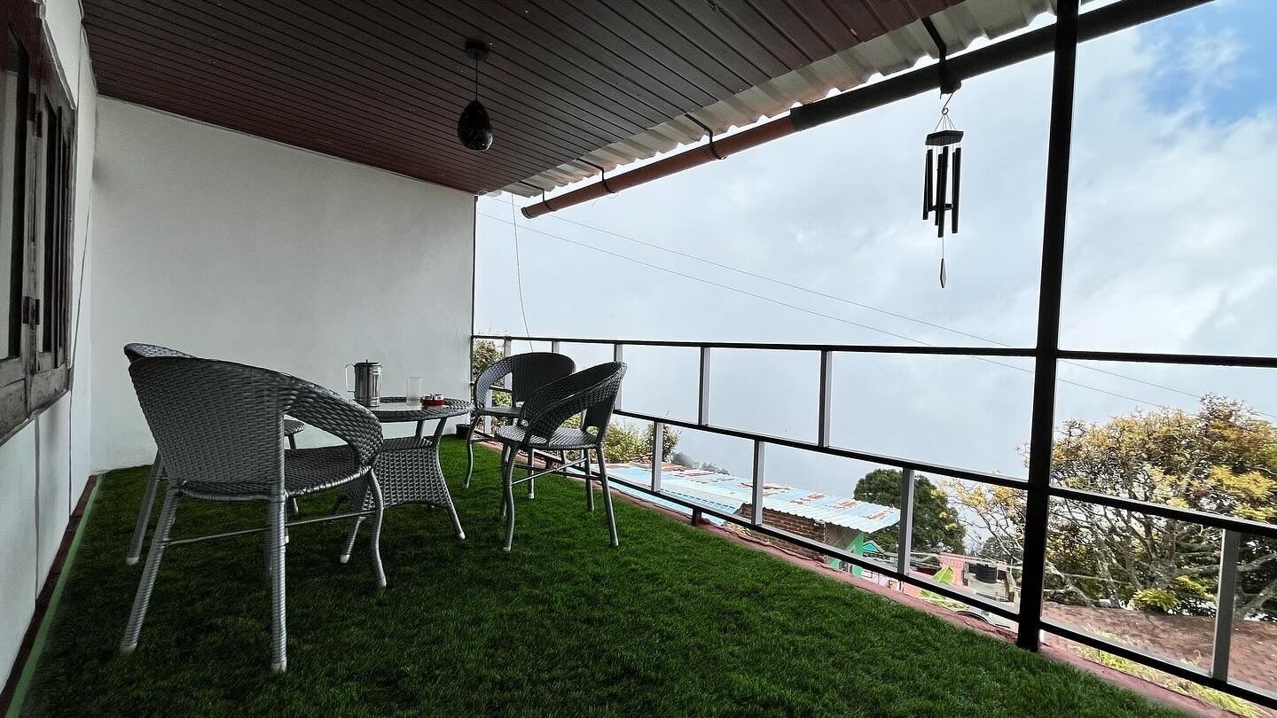 A balcony with wicker chairs and a table, overlooking a residential area.