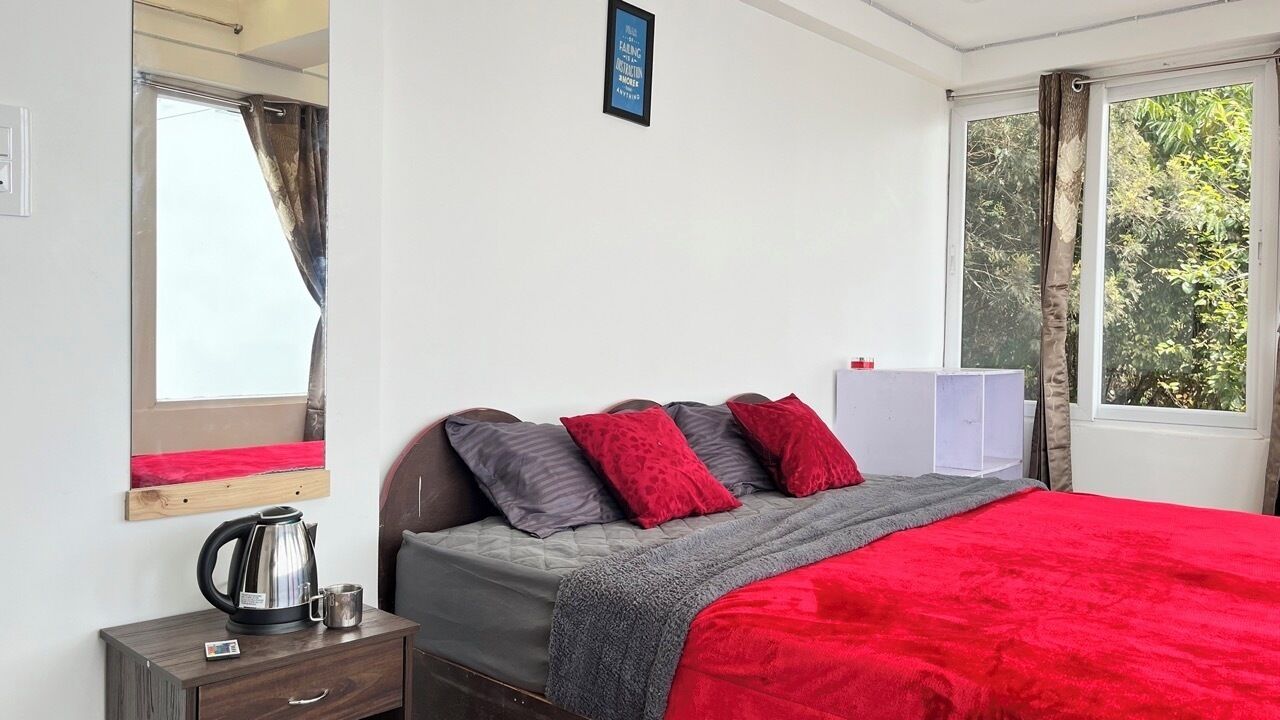 A bedroom with a bed, a nightstand, a kettle, and a window with curtains.