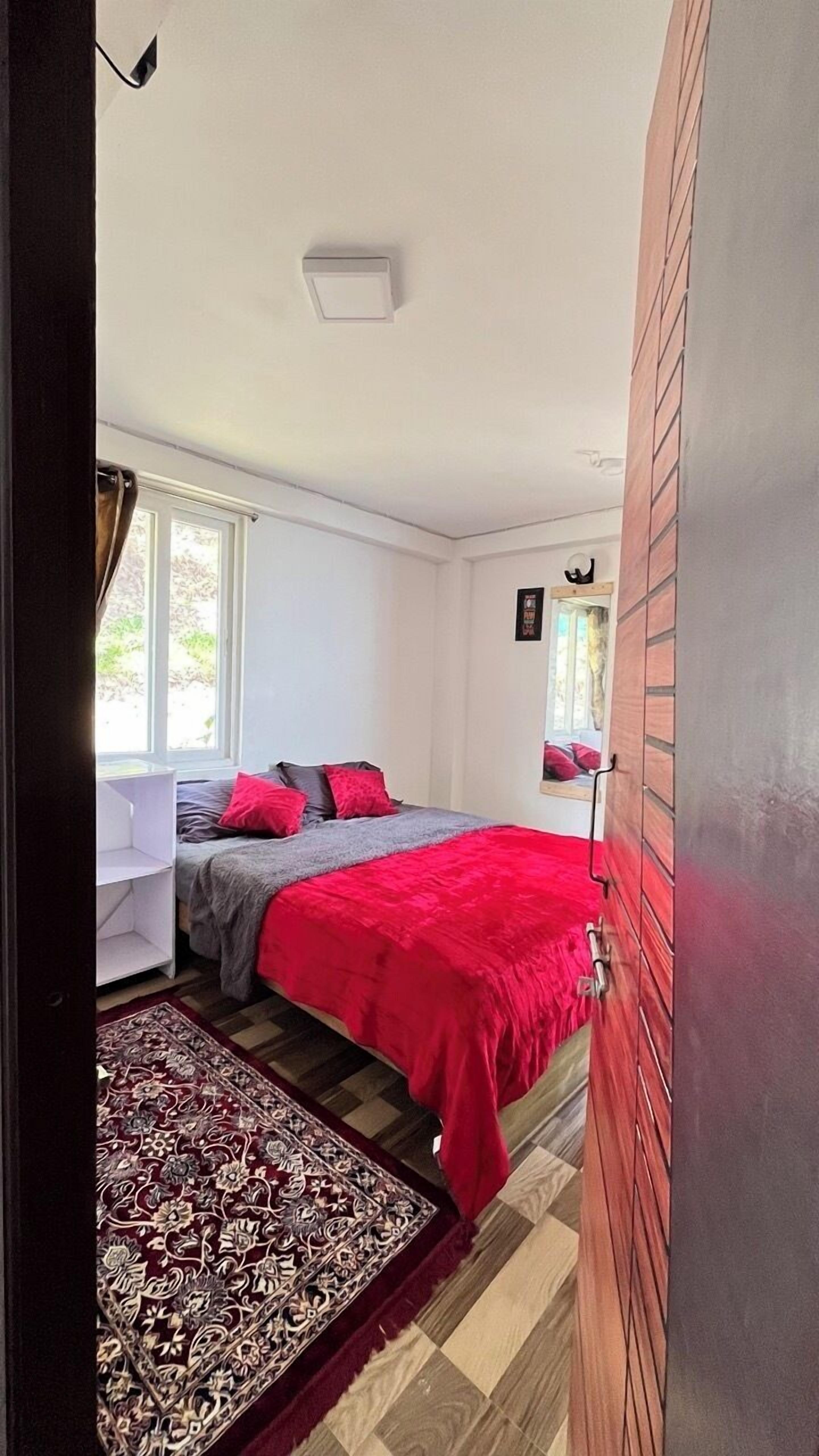 A bedroom with a bed, a bedside table, a window, and a patterned rug.