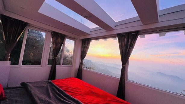 A room with a bed, large windows, and a view of mountains during sunset. - Mount Olympus Lounge (Kodaikanal)