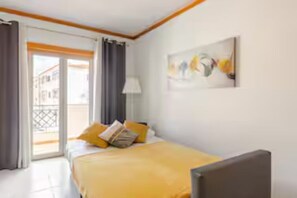 A hotel room with a bed, a painting, a window with curtains, and a view of the outside. - Sunset Apartment - Albufeira (Albufeira)