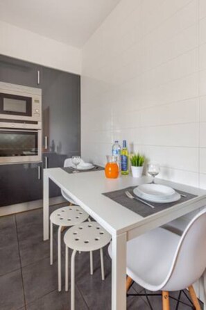 A modern kitchen with a built-in oven, a dining table with four stools, and a small potted plant on the counter. - Sunset Apartment - Albufeira (Albufeira)