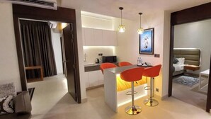 Quarto de hotel moderno com área de refeições, cozinha compacta e quarto separado.