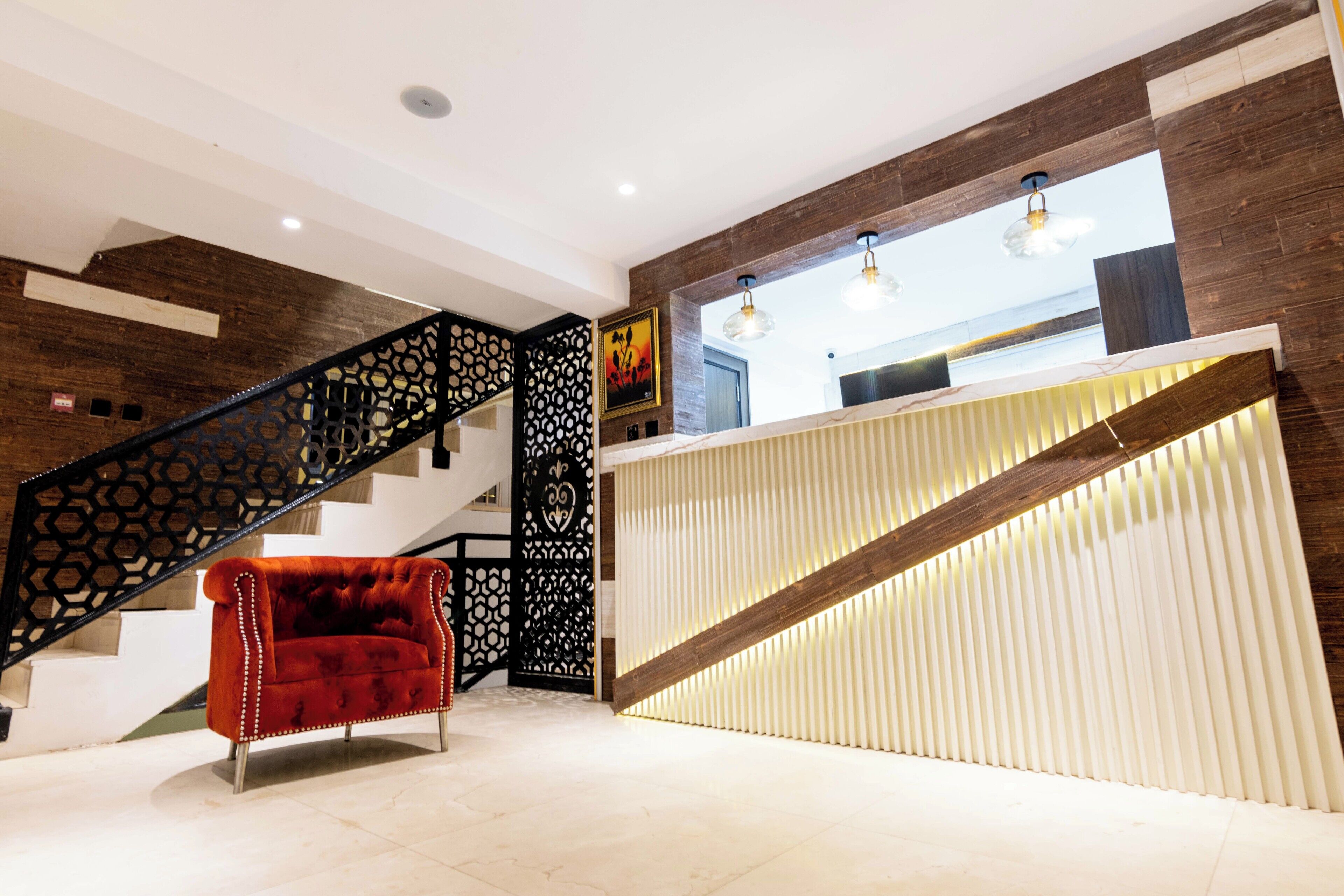 A modern reception area with a staircase, a red upholstered chair, and a wooden reception desk.