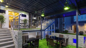 Un espacio interior moderno con una escalera, una zona de comedor con mobiliario de mimbre y un suelo de césped artificial verde.