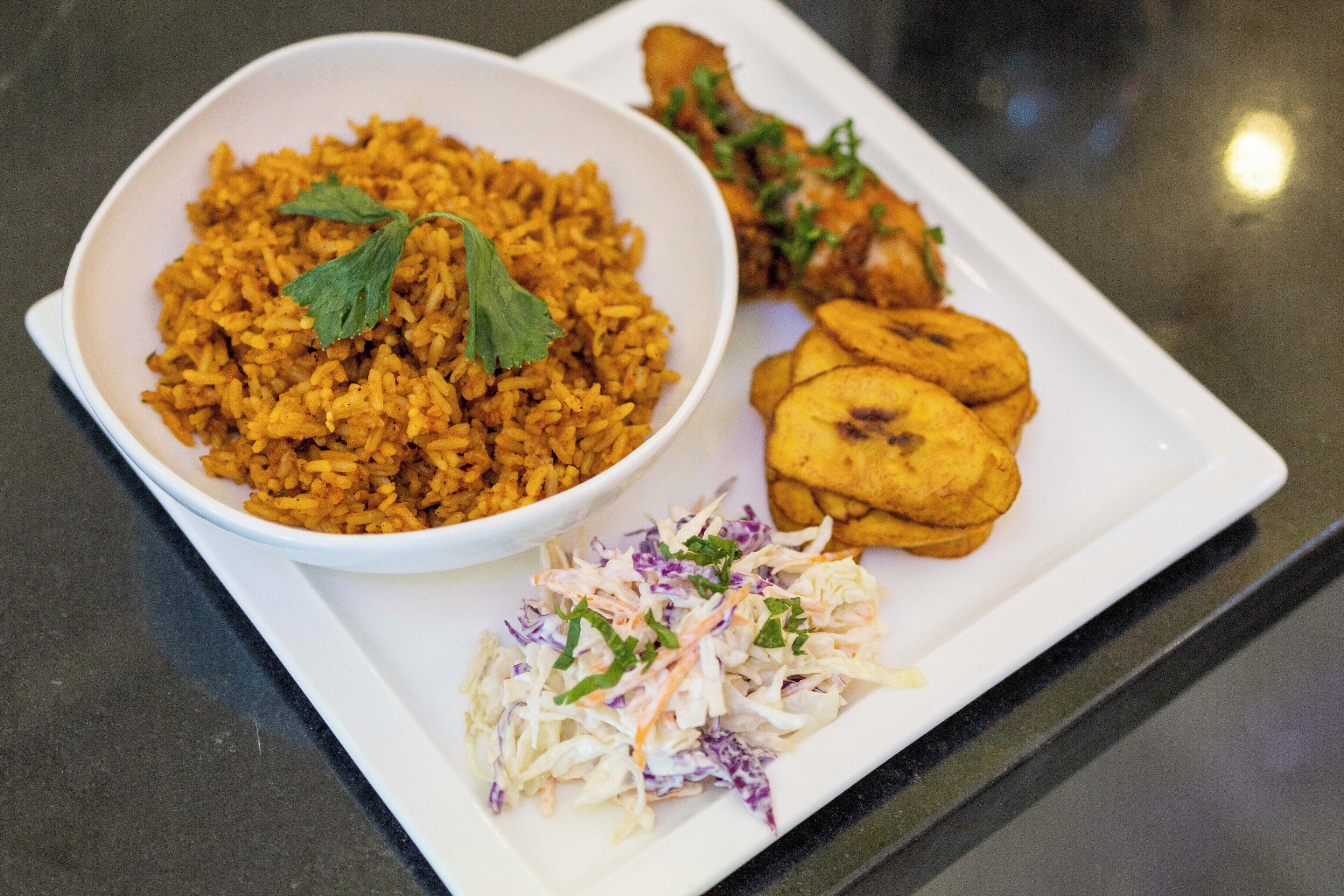 Un plato de arroz, pollo frito, plátanos maduros y ensalada de col.