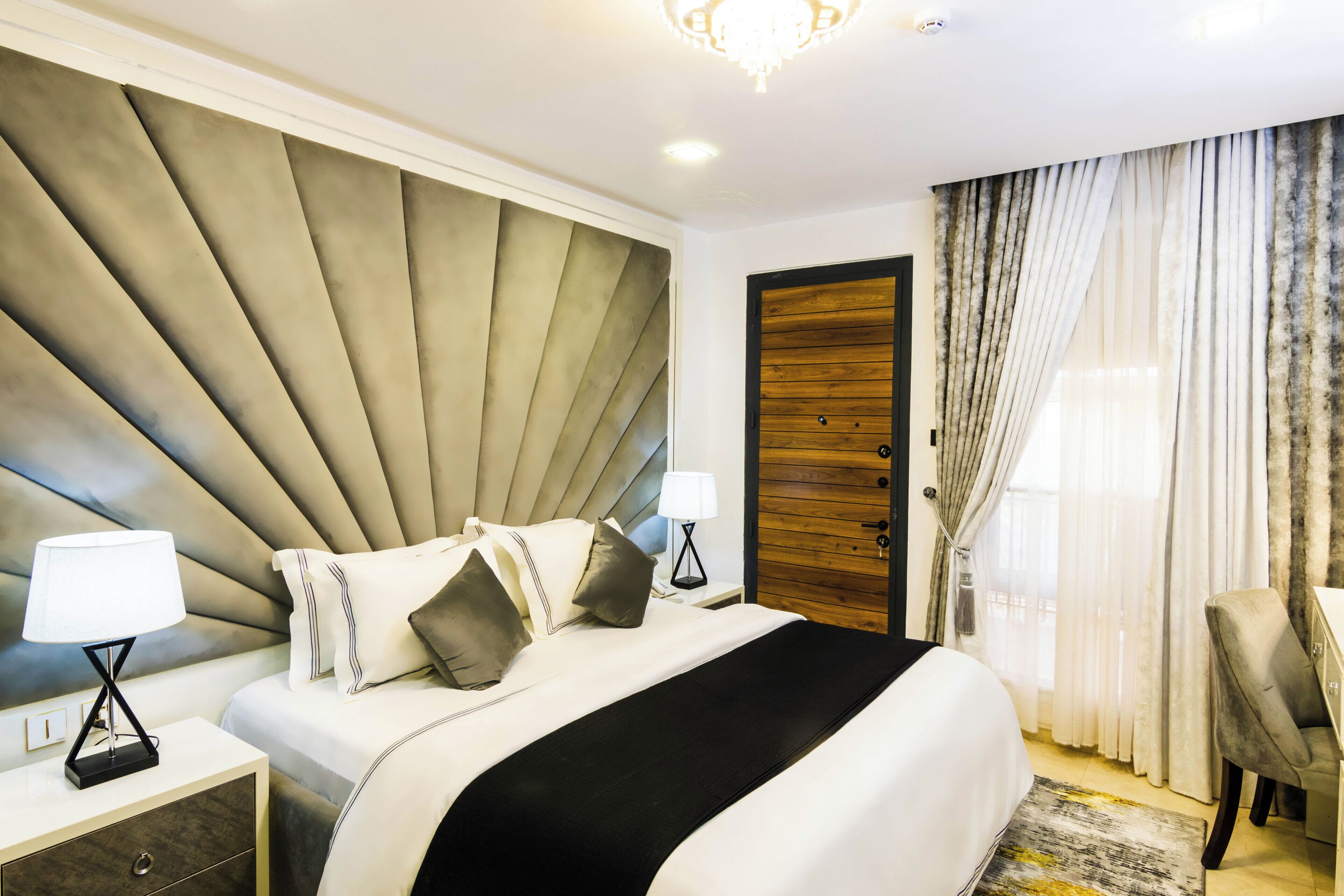 A hotel room with a large bed, a nightstand with a lamp, a wooden door, and a chair.