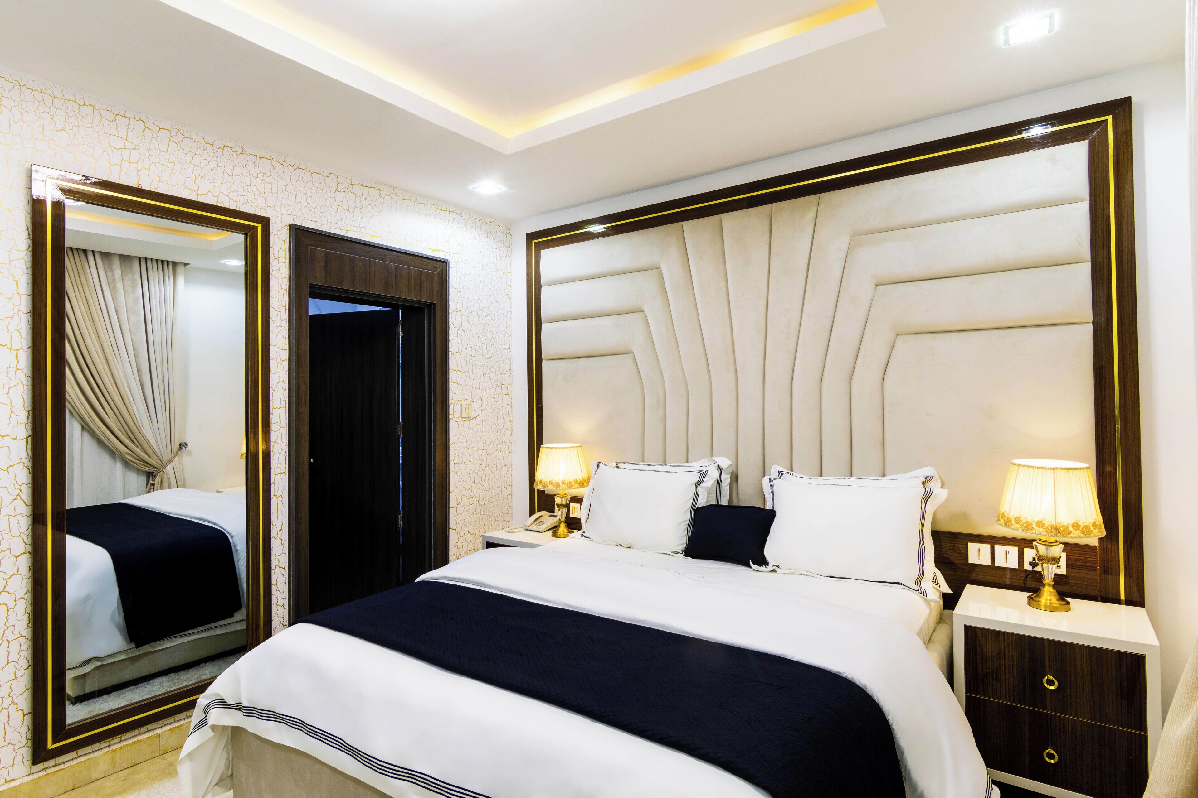A hotel room with a large bed, two bedside tables with lamps, a mirror, and a door.