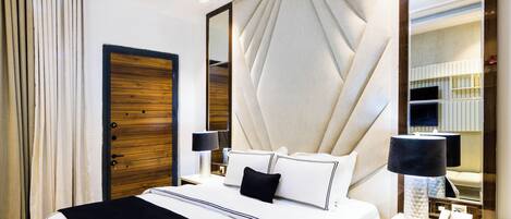 Une chambre d’hôtel avec un grand lit, une porte en bois, un miroir et une table de chevet avec une lampe.