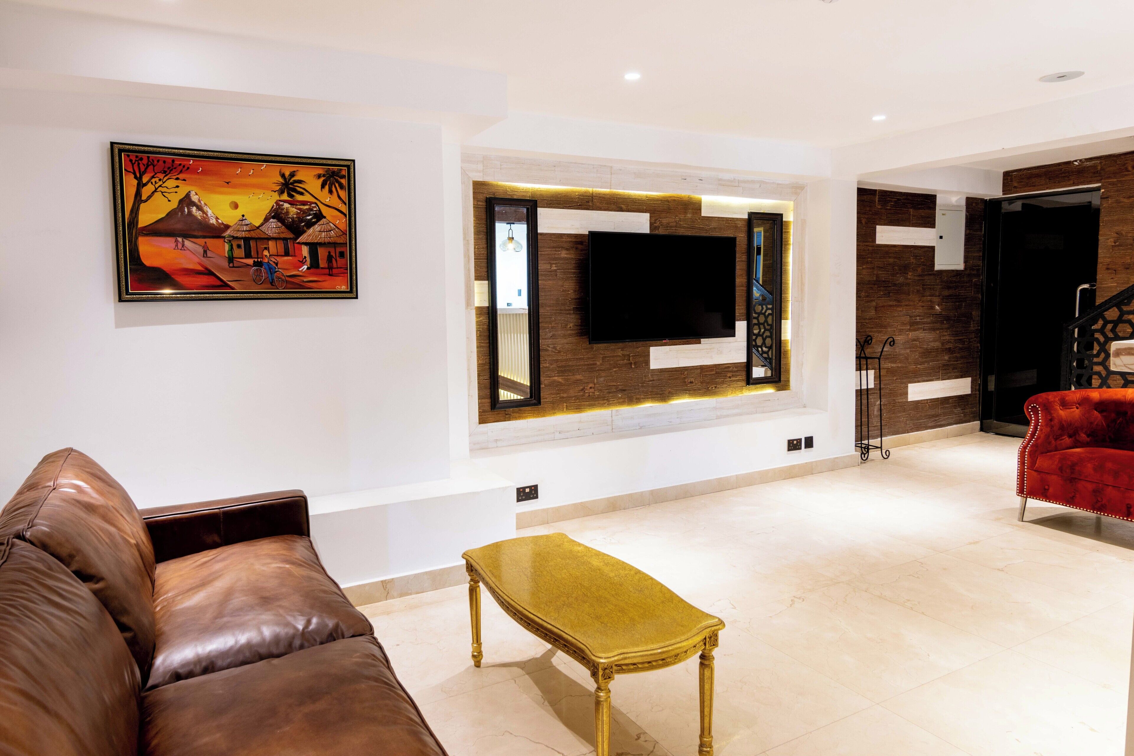 A modern living room with a leather sofa, a gold table, a mounted TV, and a painting on the wall.