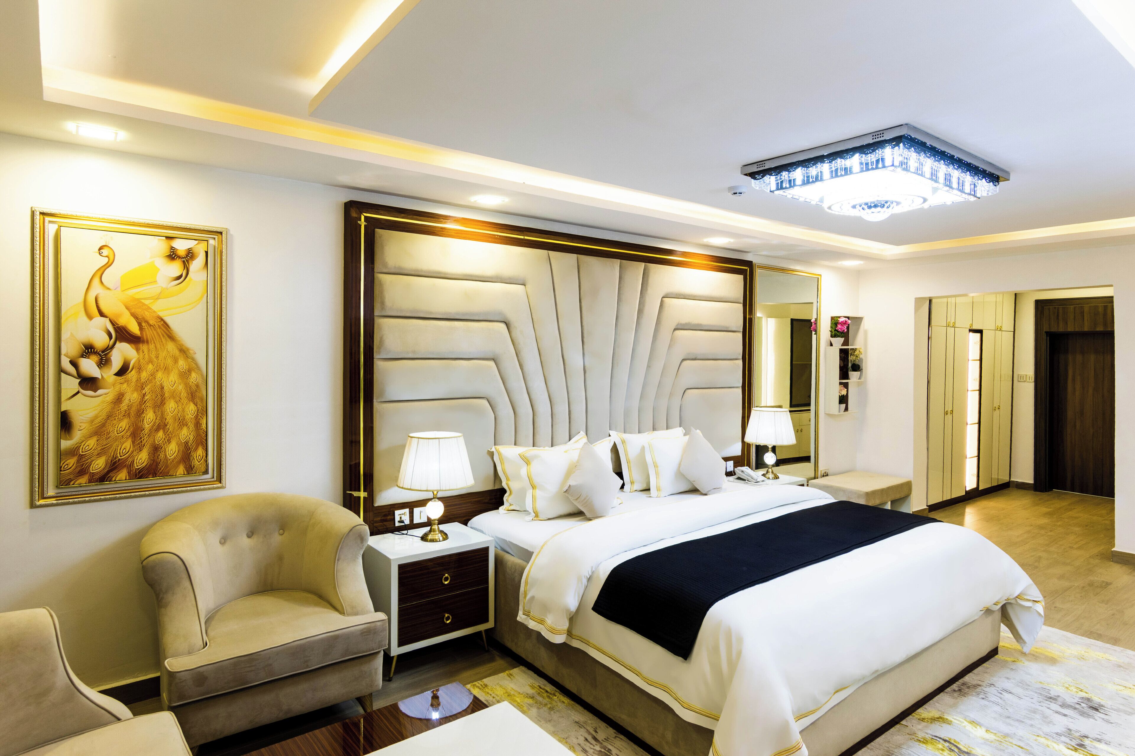 A hotel room with a large bed, a sitting area with a chair, a nightstand, and a wall-mounted mirror.