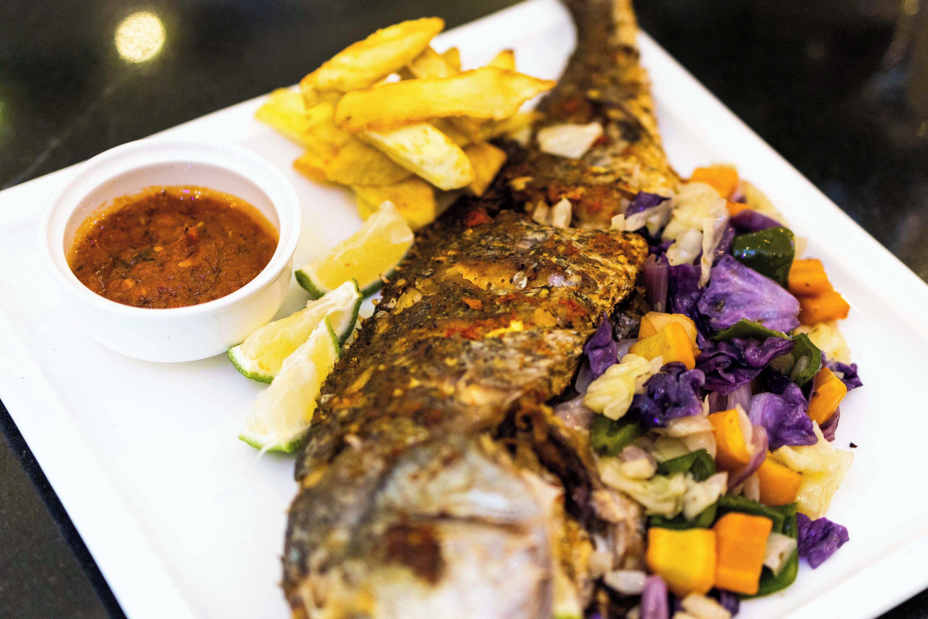 A plate with a whole fish, fries, and a side salad.