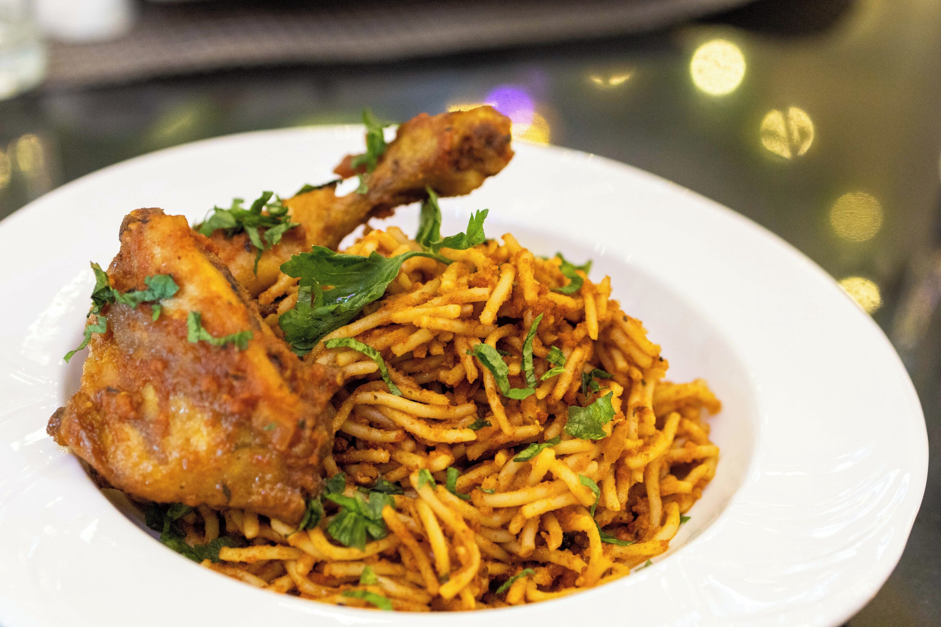 A plate of food with noodles and a piece of fried chicken garnished with herbs.