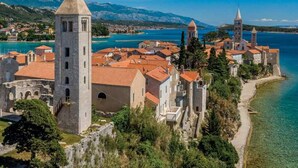 A coastal town with historic buildings, a prominent tower, and a clear view of the sea. - Apartment Belisima Delux (Rab)