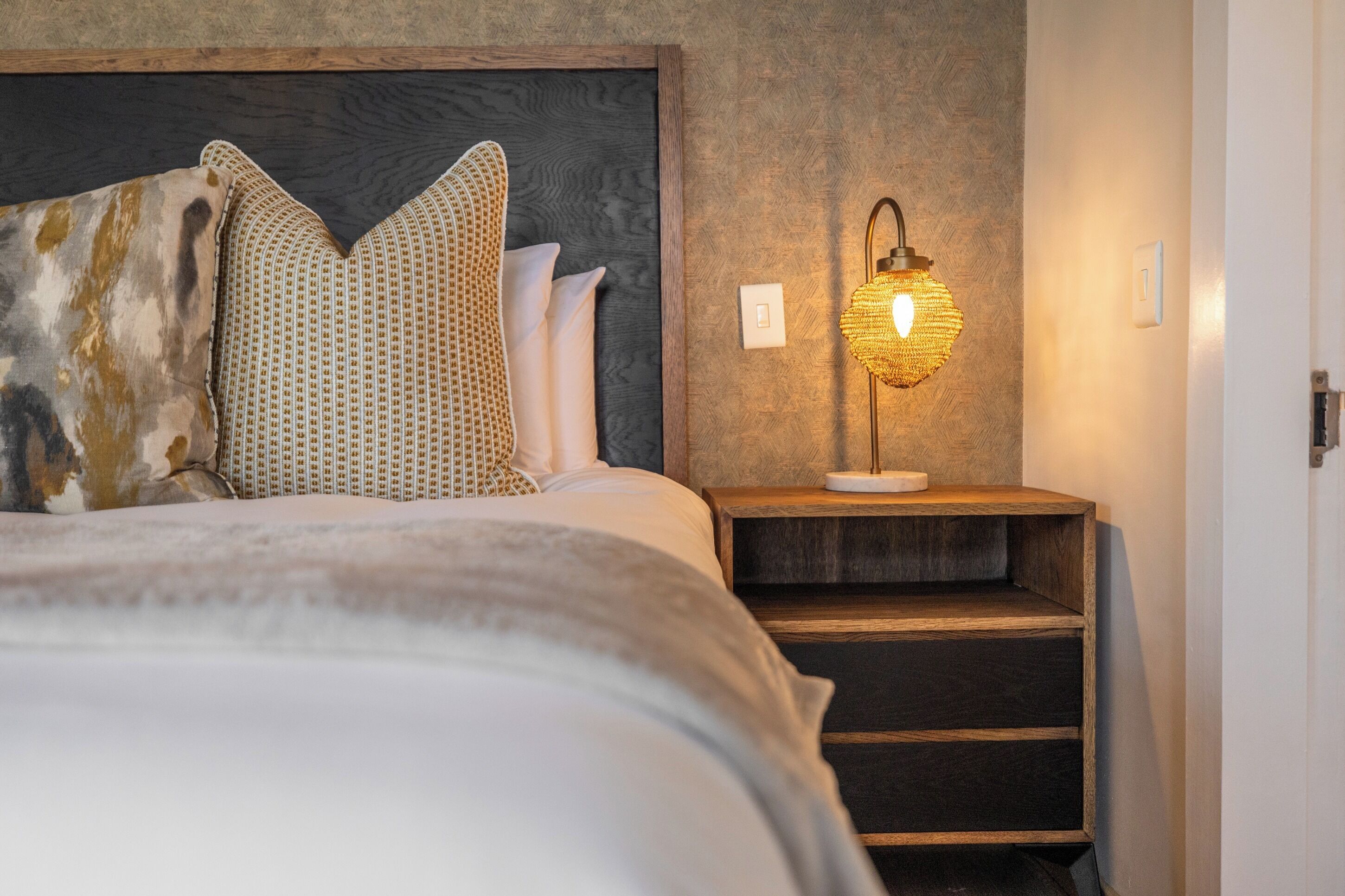 A neatly made bed with patterned pillows and a bedside lamp.