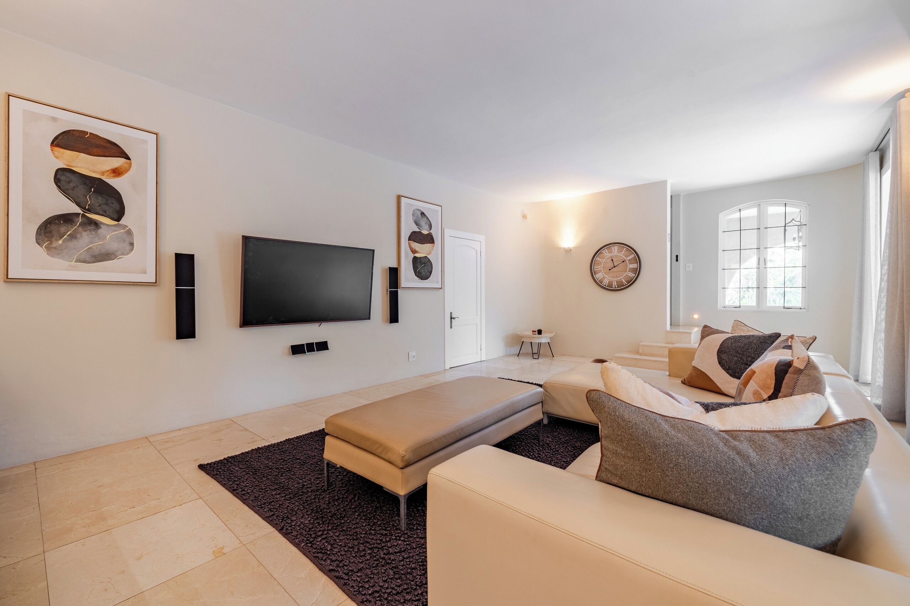 Un salon moderne avec un téléviseur à écran plat, un canapé, un banc et des œuvres d’art accrochées aux murs.