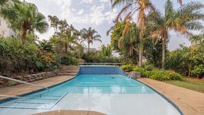 Una piscina con borde de mosaico azul, rodeada de palmeras y abundante follaje.