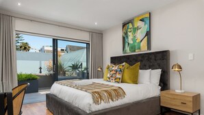 A modern bedroom with a large bed, a nightstand, a floor lamp, and a painting on the wall. - Three Bedroom Family Haven Sea Point (Cape Town)