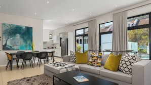 A modern living room with a sofa, coffee table, and dining area. - Three Bedroom Family Haven Sea Point (Cape Town)
