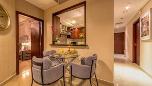 Habitación de hotel moderna con zona de comedor que incluye una mesa redonda y cuatro sillas grises. Un espejo grande refleja el interior de la habitación, y se puede ver una pequeña cocina al fondo.