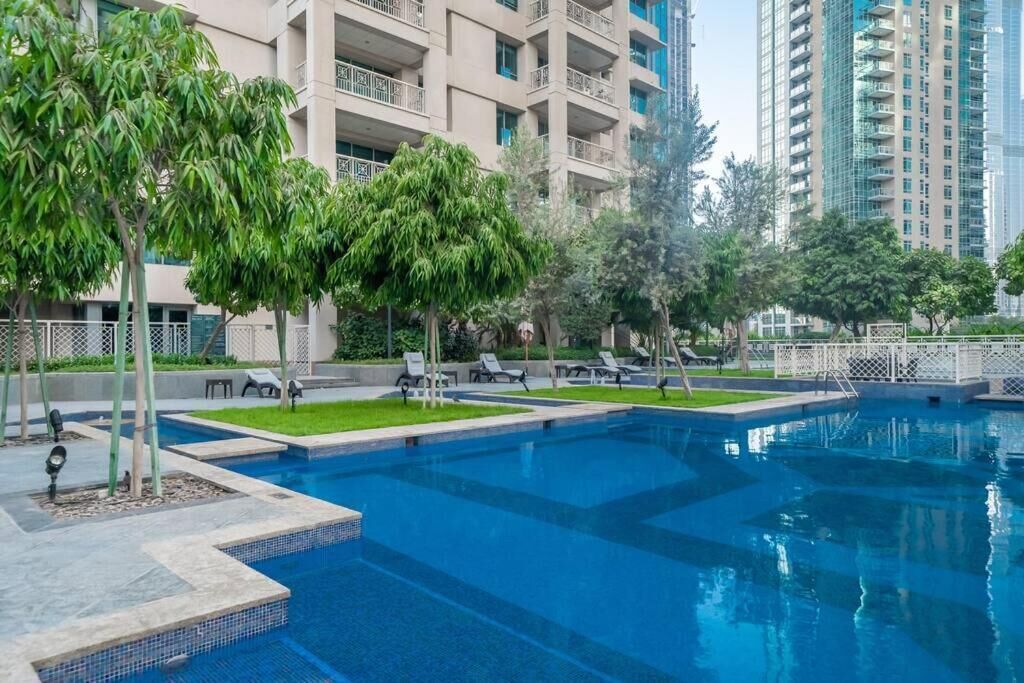A swimming pool with lounge chairs and trees, surrounded by high-rise buildings.