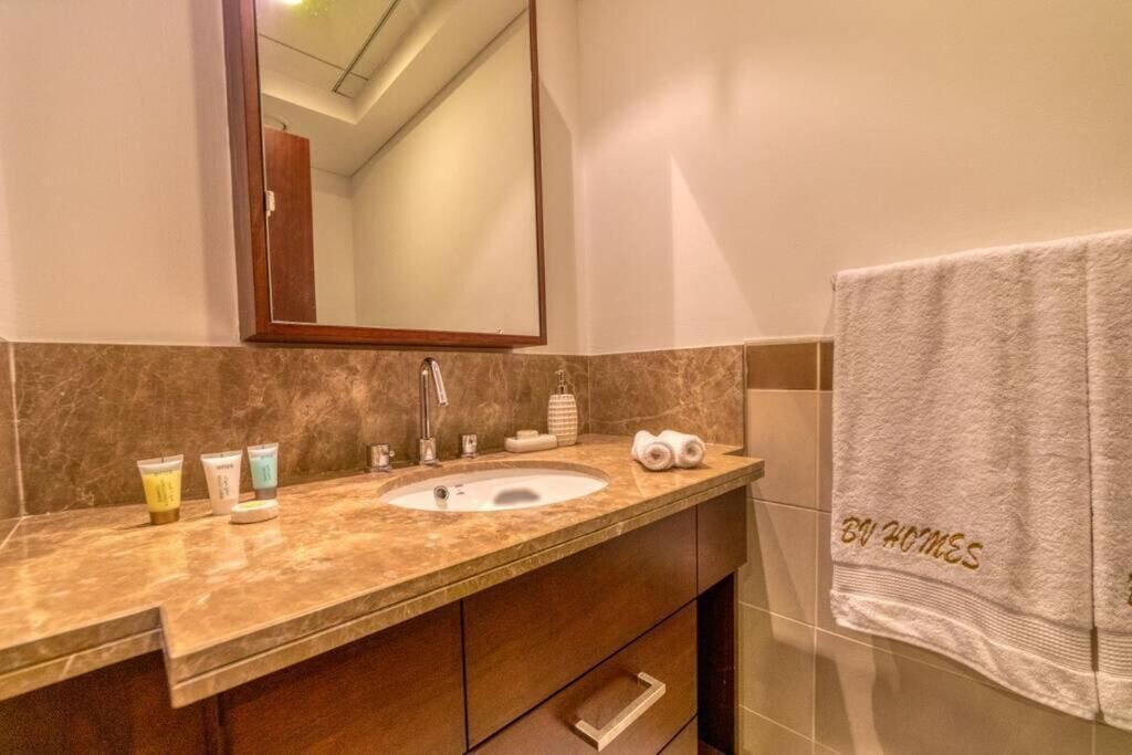 Une salle de bain avec un lavabo en marbre, un grand miroir et une serviette ornée du logo « BU HOMES » brodé dessus.
