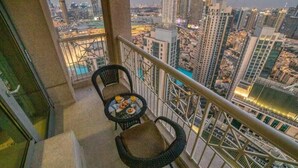 Un balcón con dos sillas y una mesa pequeña, con vista a un paisaje urbano con edificios altos.