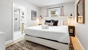 Un dormitorio con una cama grande, una mesita de noche, una lámpara de noche, una ventana con cortinas y un ventilador de techo.
