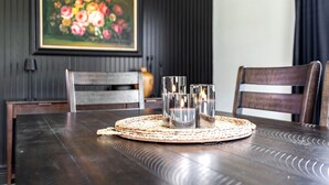 Una mesa de comedor con un mantel tejido, tres vasos y un cuadro de flores en la pared.