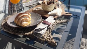 Een tafel met croissants, sinaasappelsap en een schaal gebakjes op een balkon met uitzicht op zee.