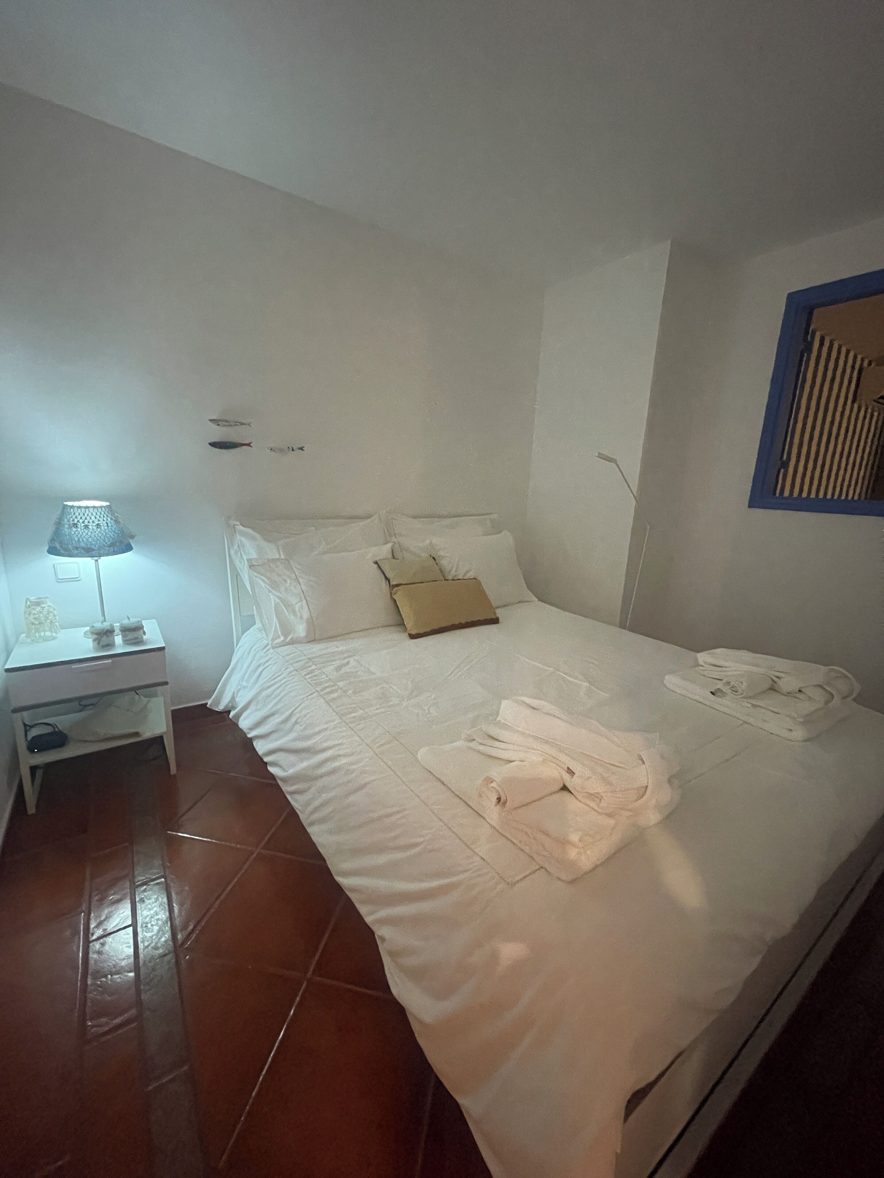 Une chambre d’hôtel avec un lit, une table de chevet, une lampe et une fenêtre avec des stores.
