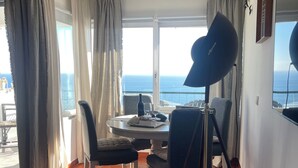 Een kamer met een eettafel, stoelen, een lamp en uitzicht op zee.