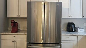 A stainless steel refrigerator in a kitchen with white cabinets and a marble countertop.